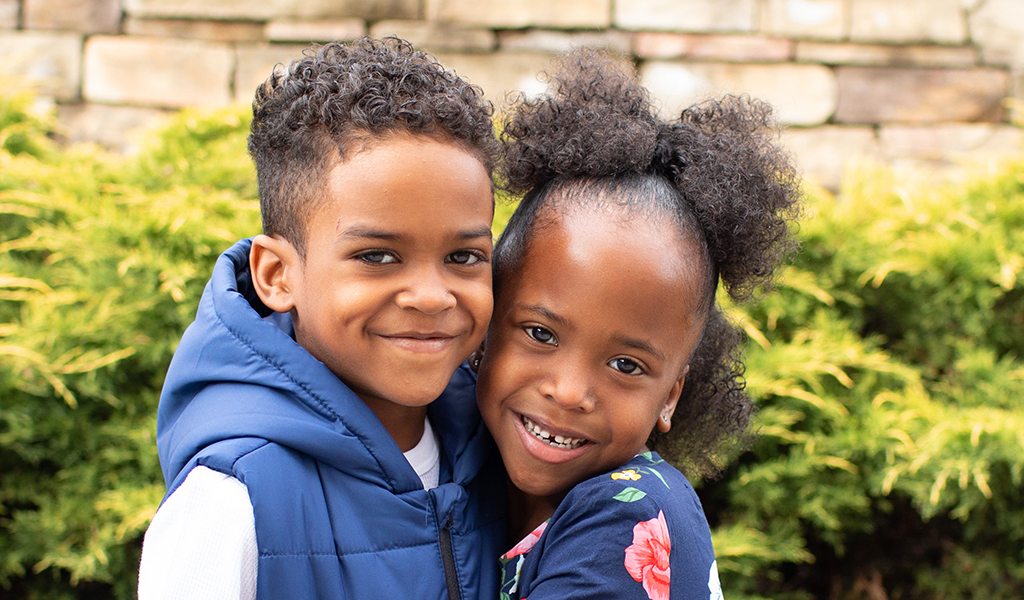 Young sister and brother outside hugging